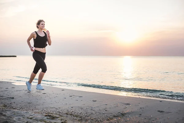 Systemem kobieta. Kobiece kobieta lekkoatletka joggingu podczas słońca na plaży. — Zdjęcie stockowe