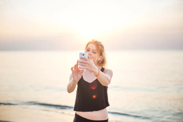 Jovem belo modelo de fitness caucasiano tirar fotos de si mesma com câmera do telefone móvel na praia — Fotografia de Stock