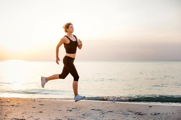 Systemem kobieta. Kobiece kobieta lekkoatletka joggingu podczas słońca na plaży. — Zdjęcie stockowe