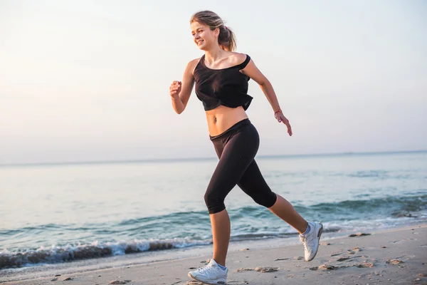 Systemem kobieta. Kobiece kobieta lekkoatletka joggingu podczas słońca na plaży. — Zdjęcie stockowe