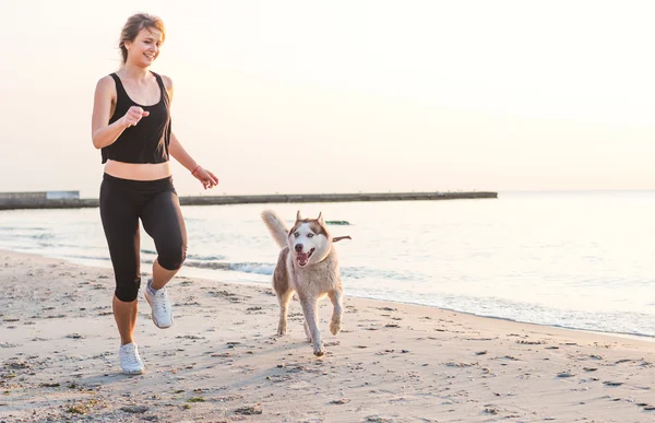 Young caucasian female playing with siberian husky dog on beach during sunrise — Stok fotoğraf