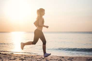 Çalışan kadın. Kadın atlet gündoğumu sırasında sahilde koşu.