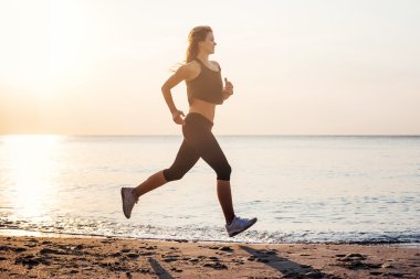 Çalışan kadın. Kadın atlet gündoğumu sırasında sahilde koşu.