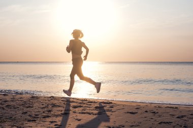 Çalışan kadın. Kadın atlet gündoğumu sırasında sahilde koşu.