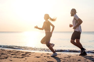 Kişi - kadın ve erkek atlet koşucular sahilde koşu çalışmıyor. Sağlıklı yaşam tarzı açık havada gündoğumu veya günbatımı sırasında egzersiz genç fitness çift uygun