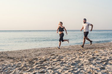 Kişi - kadın ve erkek atlet koşucular sahilde koşu çalışmıyor. Sağlıklı yaşam tarzı açık havada gündoğumu veya günbatımı sırasında egzersiz genç fitness çift uygun