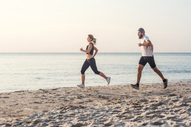 Kişi - kadın ve erkek atlet koşucular sahilde koşu çalışmıyor. Sağlıklı yaşam tarzı açık havada gündoğumu veya günbatımı sırasında egzersiz genç fitness çift uygun