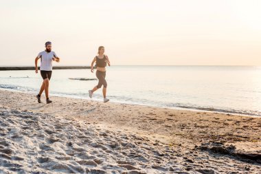 Kişi - kadın ve erkek atlet koşucular sahilde koşu çalışmıyor. Sağlıklı yaşam tarzı açık havada gündoğumu veya günbatımı sırasında egzersiz genç fitness çift uygun