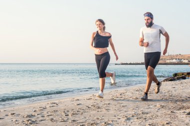 Kişi - kadın ve erkek atlet koşucular sahilde koşu çalışmıyor. Sağlıklı yaşam tarzı açık havada gündoğumu veya günbatımı sırasında egzersiz genç fitness çift uygun