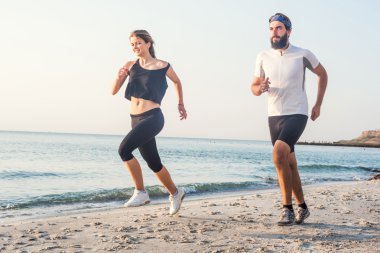 Kişi - kadın ve erkek atlet koşucular sahilde koşu çalışmıyor. Sağlıklı yaşam tarzı açık havada gündoğumu veya günbatımı sırasında egzersiz genç fitness çift uygun