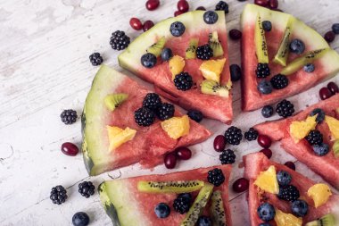 renkli tropikal meyve karpuz pizza kivi ile yaban mersini, tepesinde turuncu ve taze çilek kesimleri içine bir rustik ahşap tahta üzerinde kesmek