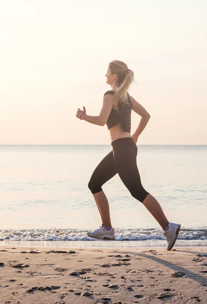 Systemem kobieta. Kobiece kobieta lekkoatletka joggingu podczas słońca na plaży. — Zdjęcie stockowe