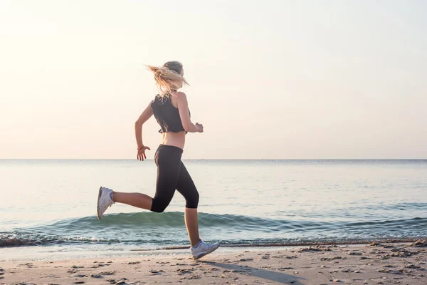 Systemem kobieta. Kobiece kobieta lekkoatletka joggingu podczas słońca na plaży. — Zdjęcie stockowe