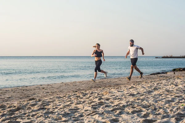 Pessoas correndo - mulher e homem atleta corredores correndo na praia. Apto jovem casal fitness exercitando estilo de vida saudável ao ar livre durante o nascer do sol ou pôr do sol — Fotografia de Stock