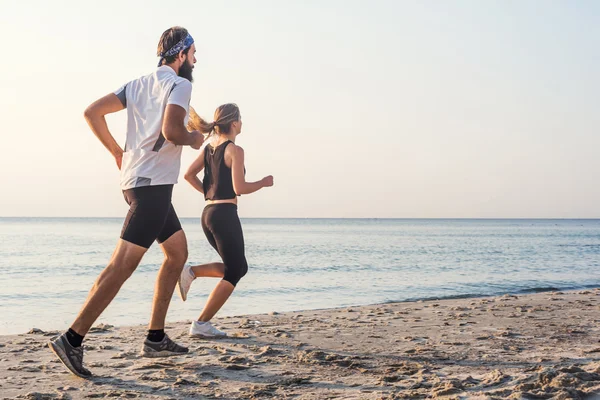 Бегущие люди - женщины и мужчины спортсмены бегают по пляжу. Подходящая молодая фитнес-пара, которая ведет здоровый образ жизни на открытом воздухе во время восхода или захода солнца — стоковое фото
