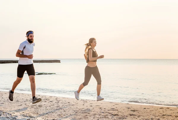 Systemem ludzi - kobieta i mężczyzna sportowiec biegaczy jogging na plaży. Zmieścić kilka młodych fitness ćwiczenia zdrowego stylu życia na zewnątrz podczas Wschodu lub zachodu słońca — Zdjęcie stockowe