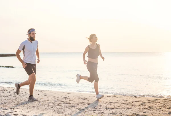 Pessoas correndo - mulher e homem atleta corredores correndo na praia. Apto jovem casal fitness exercitando estilo de vida saudável ao ar livre durante o nascer do sol ou pôr do sol — Fotografia de Stock