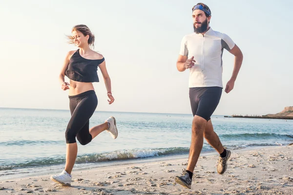 Pessoas correndo - mulher e homem atleta corredores correndo na praia. Apto jovem casal fitness exercitando estilo de vida saudável ao ar livre durante o nascer do sol ou pôr do sol — Fotografia de Stock