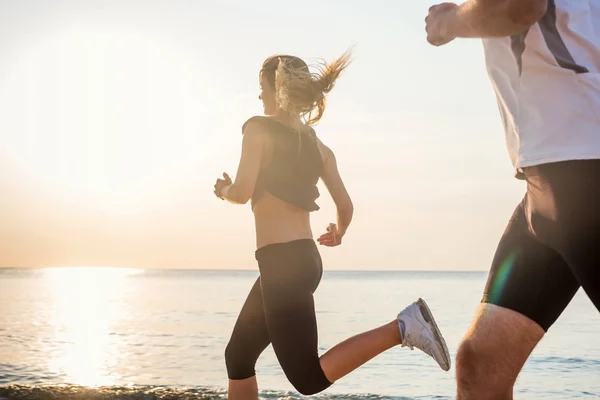 Бегущие люди - женщины и мужчины спортсмены бегают по пляжу. Подходящая молодая фитнес-пара, которая ведет здоровый образ жизни на открытом воздухе во время восхода или захода солнца — стоковое фото
