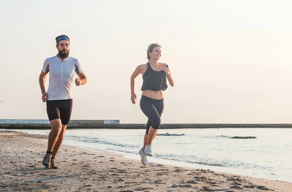Systemem ludzi - kobieta i mężczyzna sportowiec biegaczy jogging na plaży. Zmieścić kilka młodych fitness ćwiczenia zdrowego stylu życia na zewnątrz podczas Wschodu lub zachodu słońca — Zdjęcie stockowe