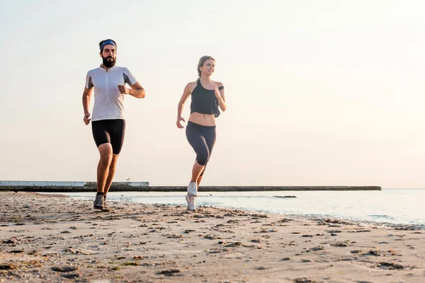 ビーチでジョギング女と男のアスリート ランナーの人々 - を実行します。日の出や日没の間に屋外健康的なライフ スタイルを行使フィットネスの若いカップルに適合します。 — ストック写真