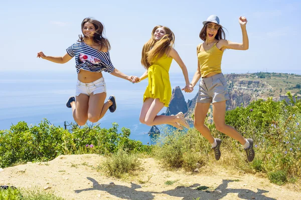 Drei junge jubelnde Freunde springen auf eine Klippe über dem Meer — Stockfoto