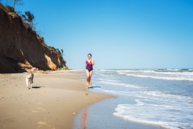 Husky köpekleri ile kız seaside köpek ile jogging sahilde, çalışan genç beyaz kadın