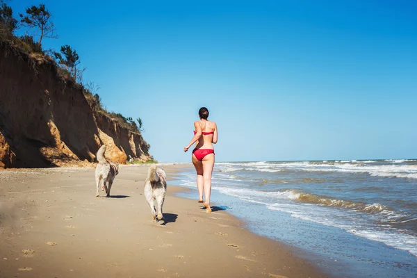 Młody kaukaski kobieta działa z psami husky na plaży, dziewczyny spacerowe nad morzem z psami — Zdjęcie stockowe