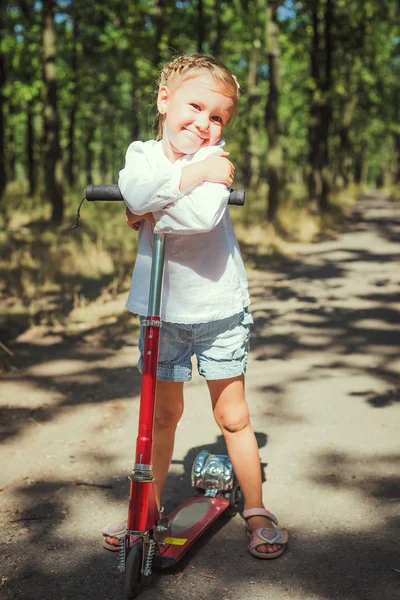 Weinig meisje paardrijden scooter in park — Stockfoto