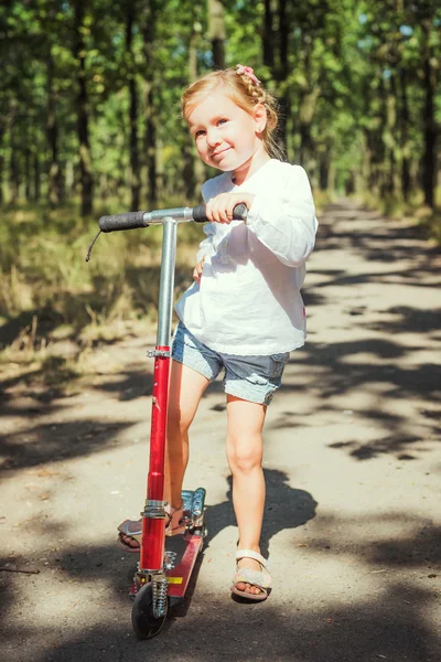 Weinig meisje paardrijden scooter in park — Stockfoto