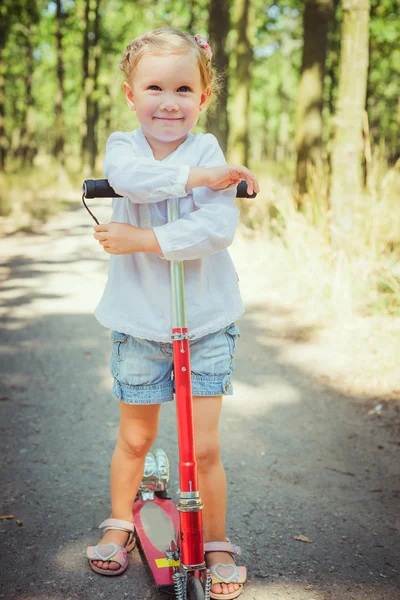 Weinig meisje paardrijden scooter in park — Stockfoto