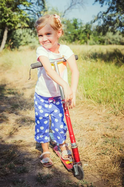 Weinig meisje paardrijden scooter in park — Stockfoto