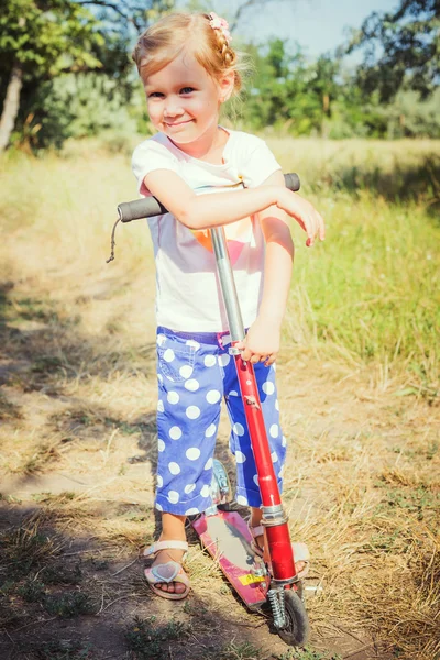 Weinig meisje paardrijden scooter in park — Stockfoto