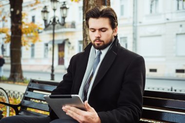 bankta oturan ve tablet açık havada kullanma bisiklet ile genç beyaz işadamı