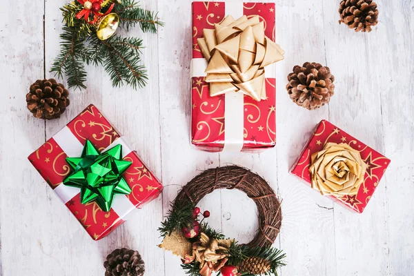 Weihnachtsdekoration mit verpackten Geschenken, Tannenzapfen und Glocken auf weißem Holzgrund — Stockfoto