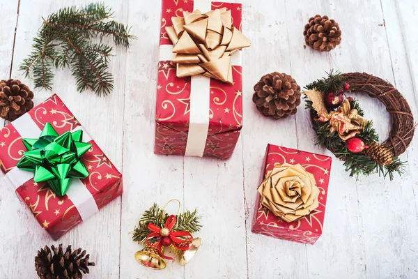 Weihnachtsdekoration mit verpackten Geschenken, Tannenzapfen und Glocken auf weißem Holzgrund — Stockfoto