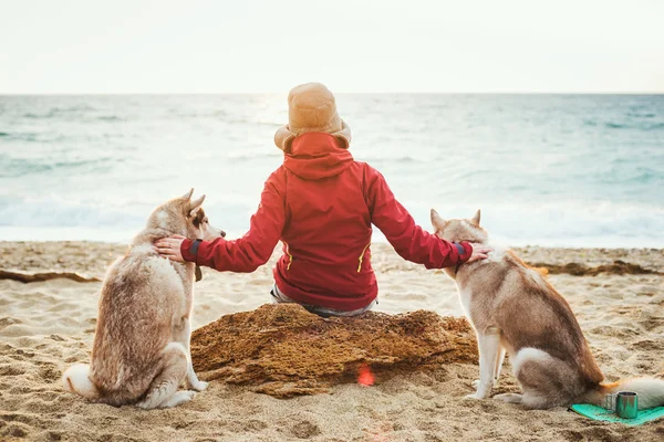 Γυναίκα που κάθεται στην παραλία με δύο σκυλιά χάσκι κατά την Ανατολή του ηλίου — Φωτογραφία Αρχείου