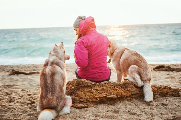 Kvinna sitter på stranden med två husky hundar under sunrise — Stockfoto