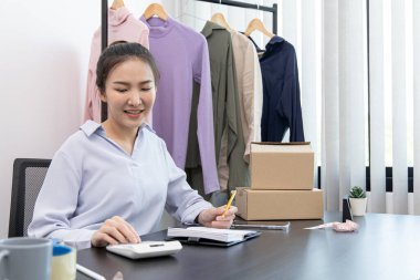 Yüzü gülen Asyalı kadın müşterilerin moda siparişlerini not alıyor, iyi hissettiriyor, sosyal medyada kıyafet satma işi ya da internetten satış, sosyal mesafede yeni iş..