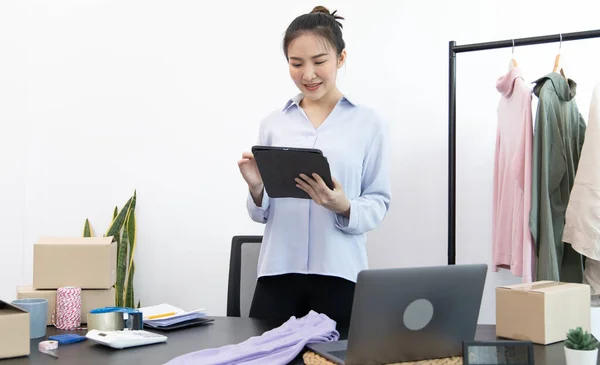 Genç Asyalı bir kadın, kıyafetlerini internetten tabletle almak isteyen bir müşteriye gülümseyerek sohbet ediyor ve anlaşmayı, sosyal medya alışverişini veya internet alışverişini onaylıyor..