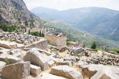 Delfon Yunanistan 'daki harabeler, arka planda taş bir duvar, mermer bir tapınak, dağlar ve ağaçların kalıntılarını görebilirsiniz.