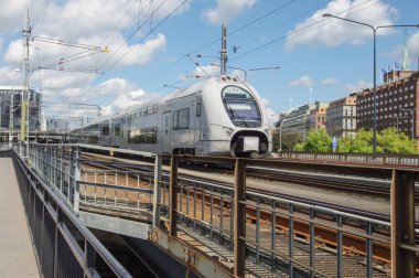 İsveç 'te çift katlı elektrikli tren, demiryolu hatlarının iki demiryolu ile ayrıldığı yerde, bazı binalar arka planda görülebilir, hepsi güneşli bir günde ve bulutlu bir günde.