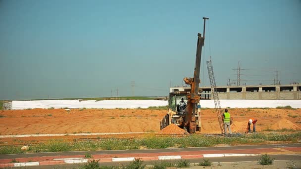 El tractor levanta una varilla de acero y la pone en un agujero en el suelo. Trabajadores de la construcción lo están ayudando . — Vídeo de stock