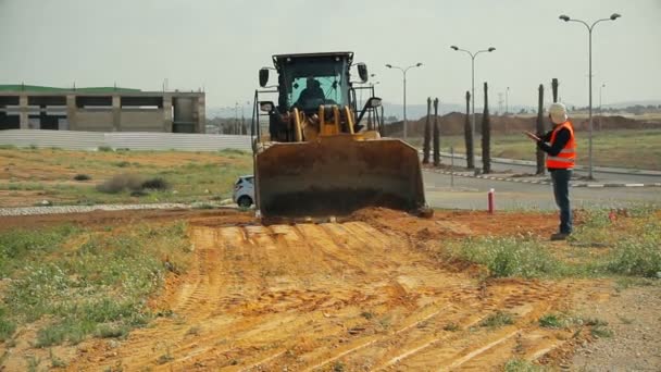 Trator com um bulldozer solo em movimento em um canteiro de obras — Vídeo de Stock