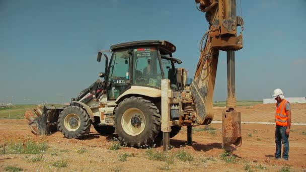 Traktor egy építkezésen fúrási készülékkel. Vállalkozó felügyelő neki. — Stock videók