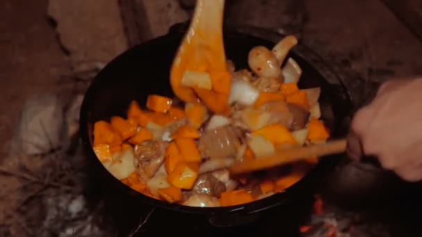 Cooking meal in cauldron on burning campfire at night — Stock Video