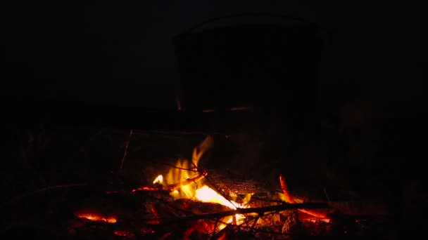 Готовить еду в котле на горящем костре ночью — стоковое видео