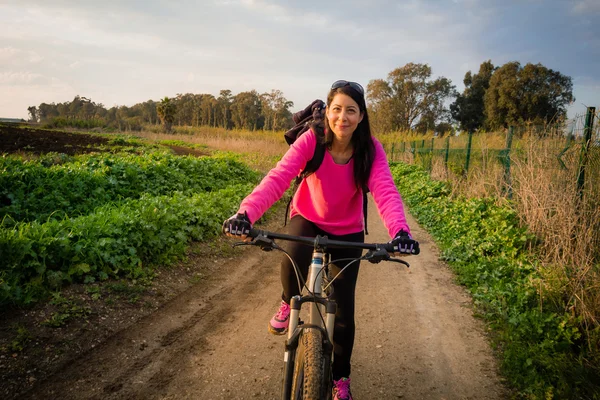 Mulher andando de bicicleta no campo e olhando para a câmera — Fotografia de Stock