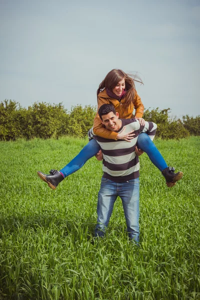 Pareja joven divirtiéndose juntos en el campo verde. La mujer cabalga — Foto de Stock