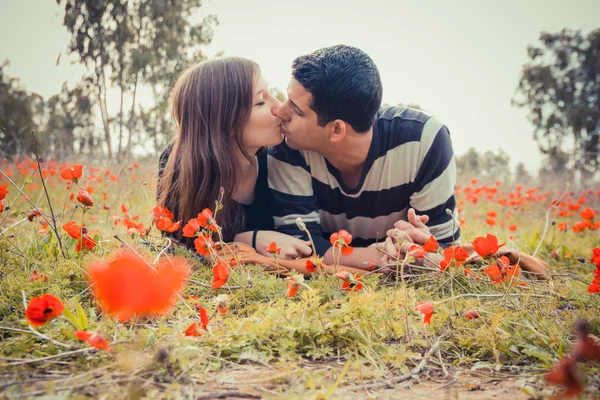 Pareja joven besándose mientras yacía en la hierba en un campo de rojo — Foto de Stock